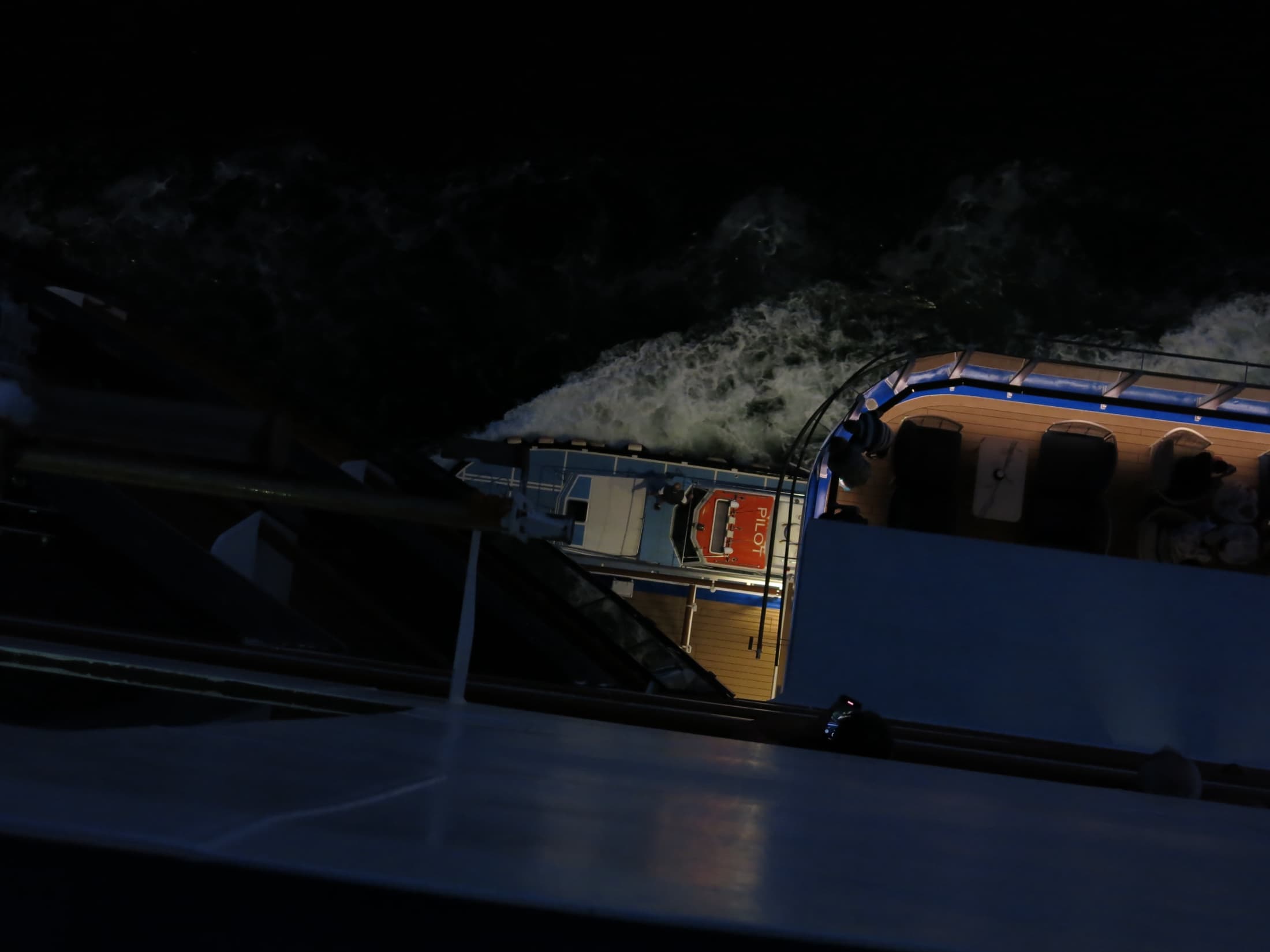 A working pilot boat glimpsed between ships during a night journey