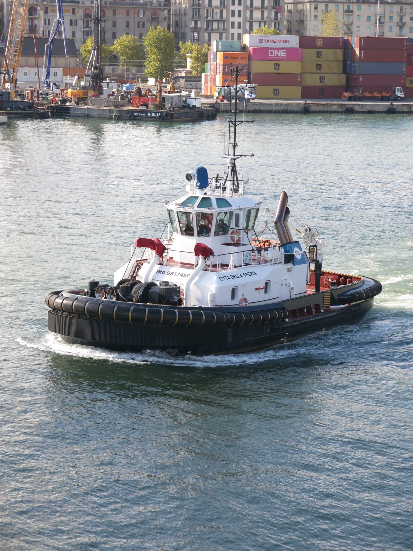 Working tug boat moving through a busy commercial harbour