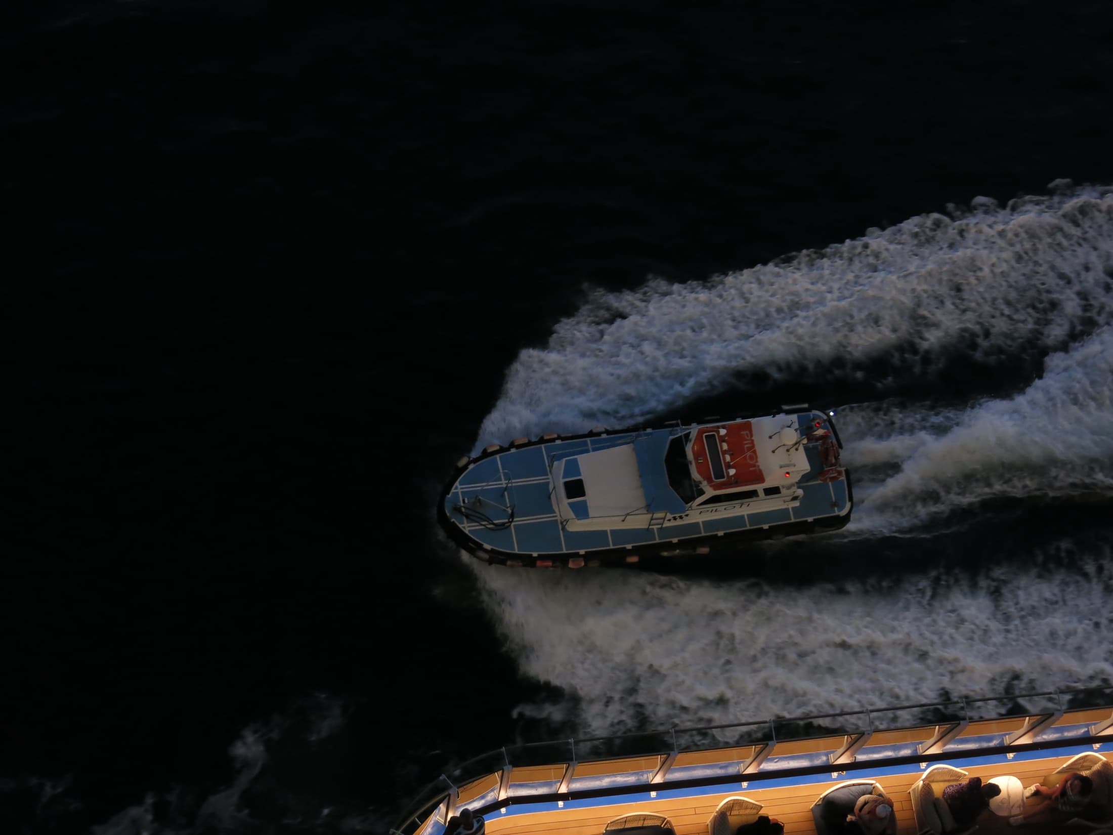 Pilot boat carving a white wake through dark water beside a ship