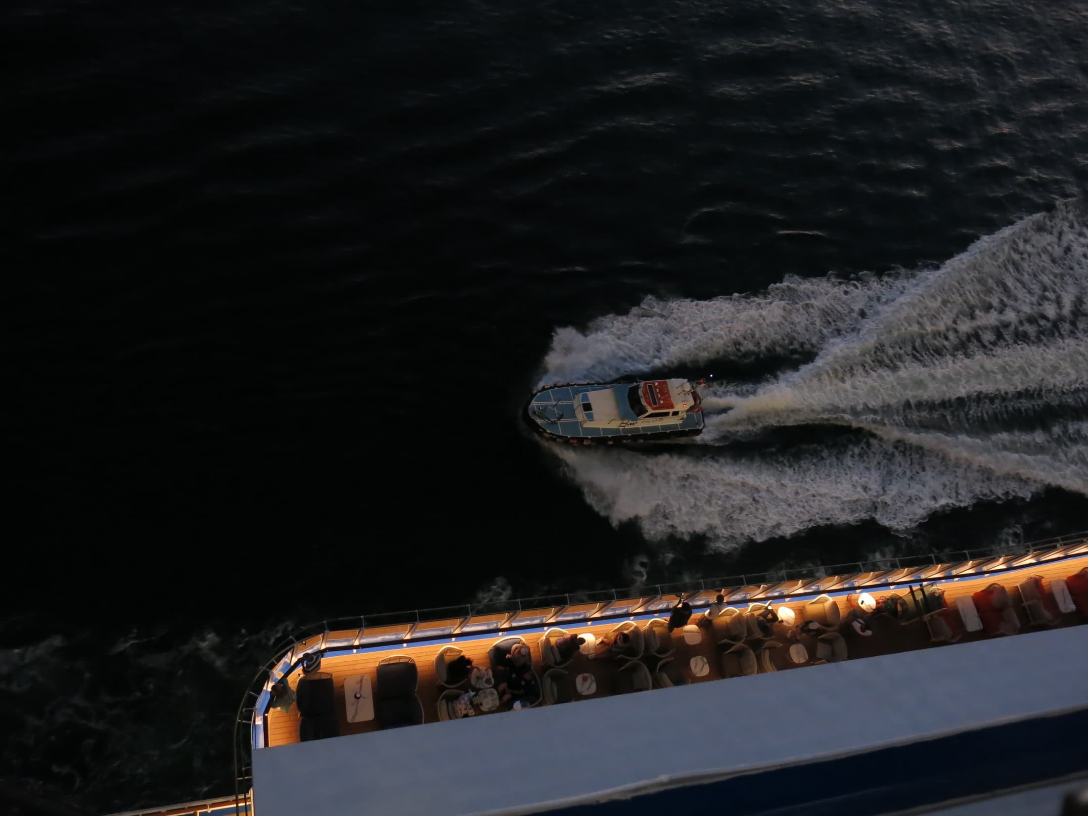 Pilot boat turning away beside the illuminated edge of a larger ship